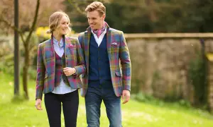 Ein Paar spaziert im Freien, beide tragen farbenfrohe Tweed-Sakkos. Sie zeigen, wie man ein Tweed-Sakko kombinieren kann, mit Westen und Jeans.