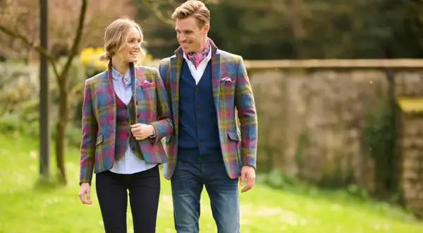 Ein Paar spaziert im Freien, beide tragen farbenfrohe Tweed-Sakkos. Sie zeigen, wie man ein Tweed-Sakko kombinieren kann, mit Westen und Jeans.