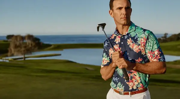 Ein Mann mit einem bunten Polohemd und einem Golfschläger auf einem Golfplatz.