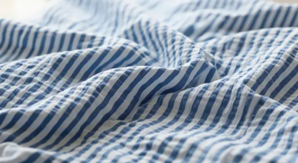 Blau-weißer Seersucker-Stoff mit charakteristischen Falten. Dieses Gewebe ist leicht und luftig, ideal für Sommerkleidung.