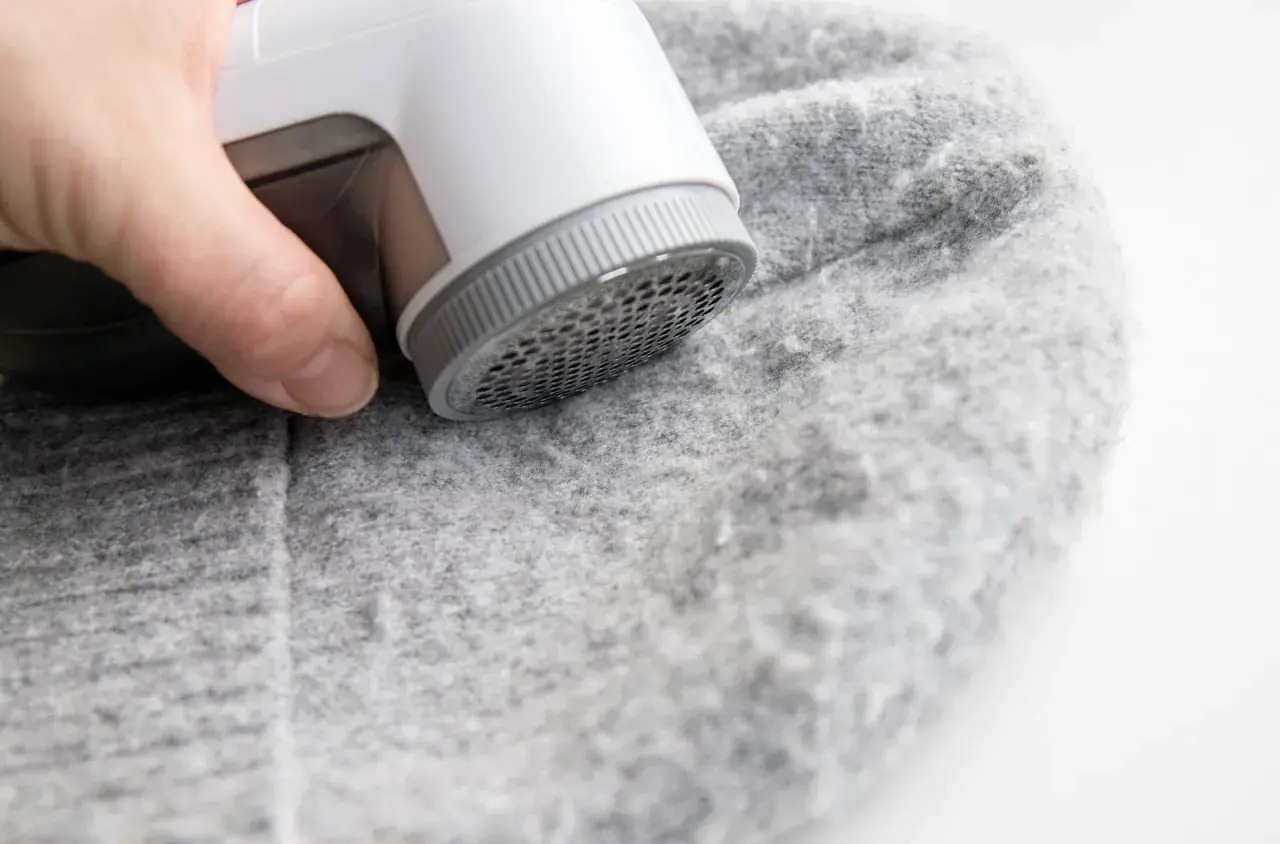 Ein Wollpullover, der eingelaufen ist, wird mit einem Fusselrasierer von Knötchen befreit.