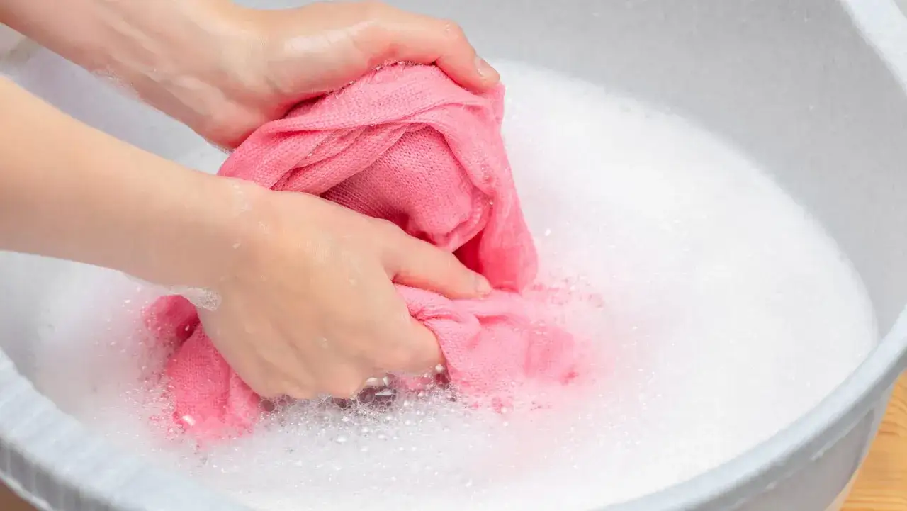 H&auml;nde waschen einen rosafarbenen Pullover in schaumigem Wasser. Ein sanfter Wollprogramm-Waschgang ist ideal f&uuml;r solche empfindlichen Textilien.