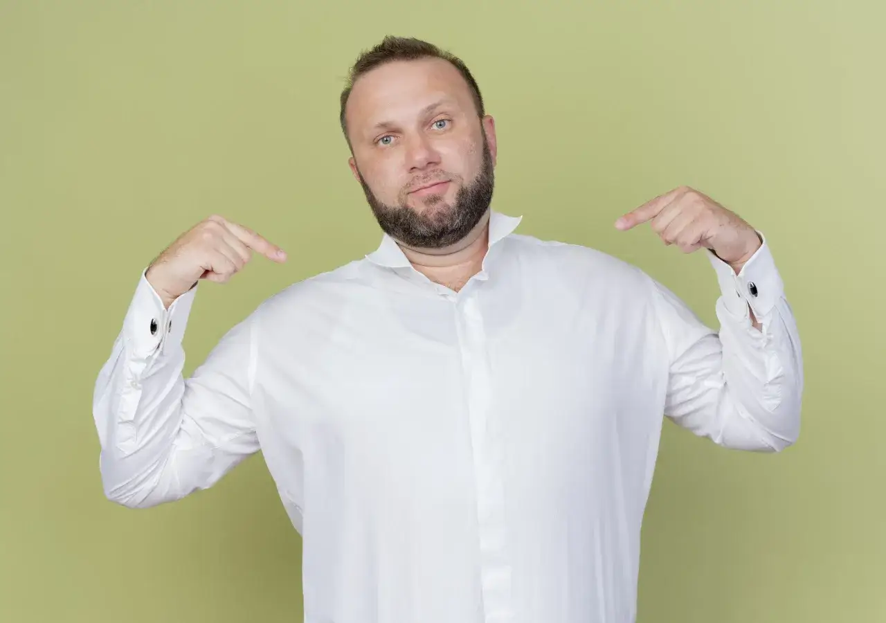 Mann zeigt auf sich und sein weißes Hemd. Er fragt sich, welches Unterhemd unter dem Hemd am besten aussieht.