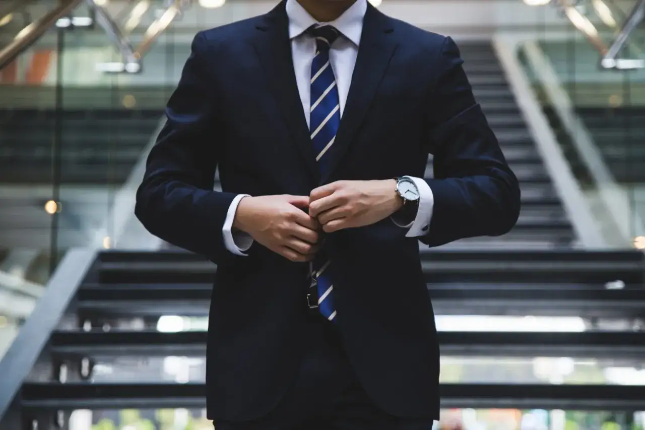 Mann im dunklen Anzug mit blau-wei&szlig; gestreifter Krawatte, der seinen blauen Blazer kombiniert.