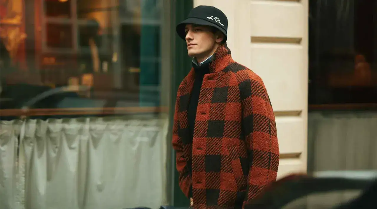 Mann im karierten Jackett und Fischerhut, ein Look im mode 90er jahre Stil, steht vor einem Schaufenster.