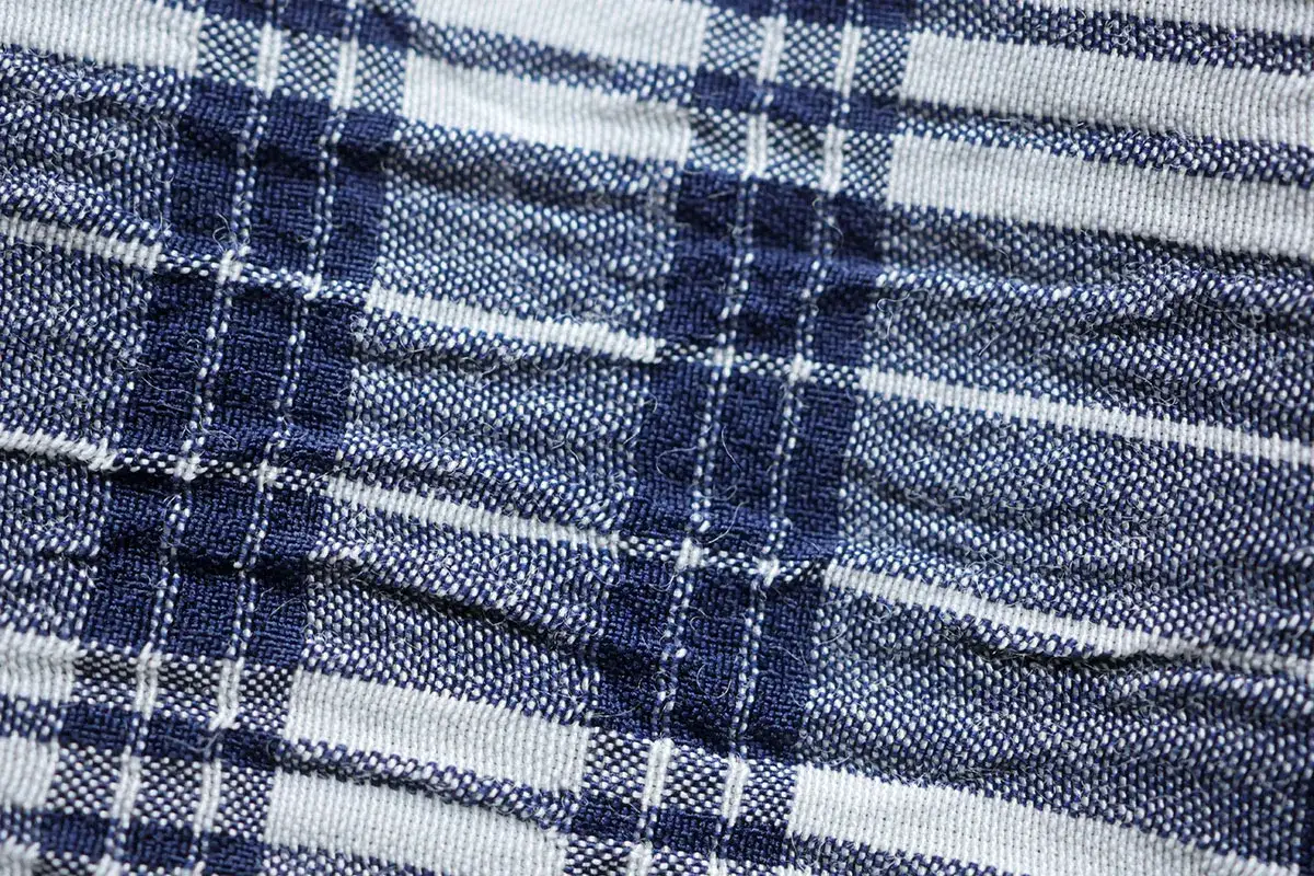 Nahaufnahme eines blauen und weißen karierten Stoffes. Die Textur ist leicht zerknittert, was typisch für Seersucker ist.
