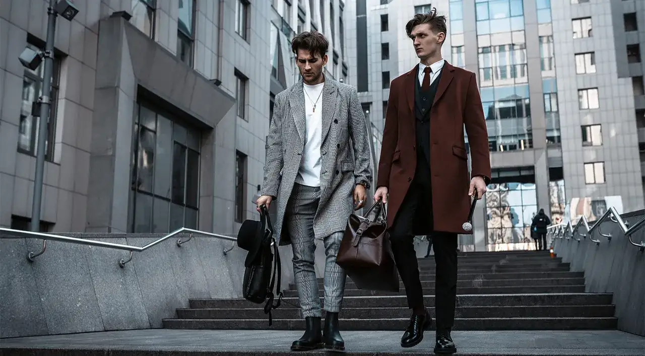 Zwei Männer in smart business attire gehen eine Treppe hinauf. Einer trägt einen karierten Mantel, der andere einen braunen Mantel.