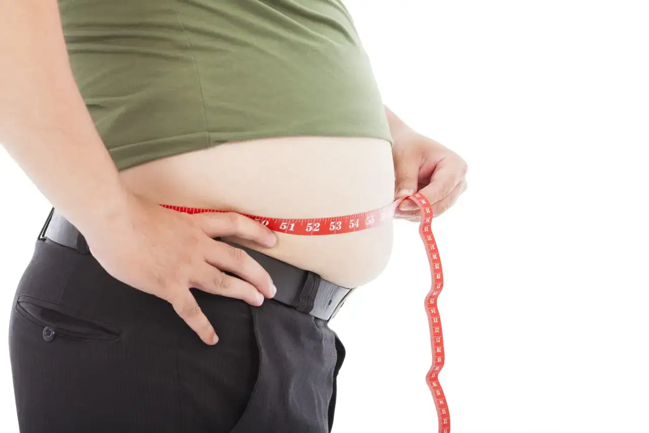 Mann misst seinen Bauch mit einem Maßband. Der Wunsch, den Bauch zu kaschieren, wird durch die Messung deutlich.