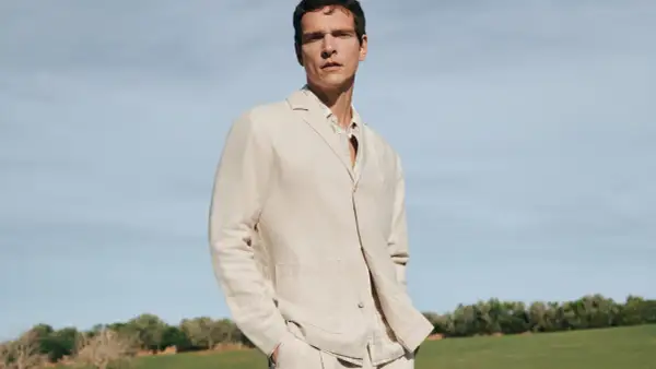 Mann in beigem Sakko und kariertem Hemd, lässig mit den Händen in den Hosentaschen. Perfekt, um ein beiges Sakko zu kombinieren für einen stilvollen Look.
